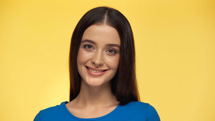 young brunette woman in blue t-shirt smiling and looking at camera isolated on yellow.