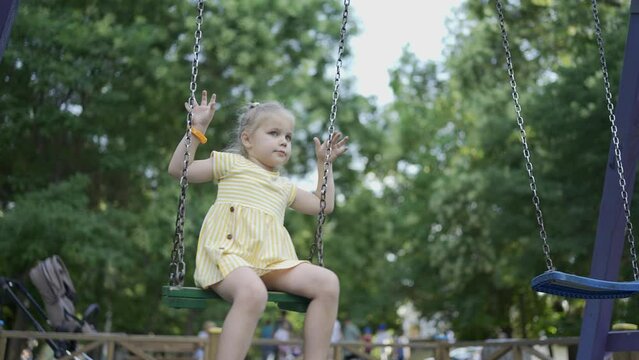Cute little girl rides on a swing in the playground. Child girl playing on the playground in the city park