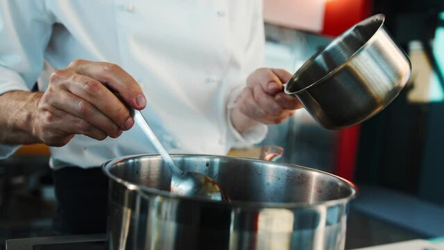 The chef makes sauce in a saucepan in professional restaurant kitchen. The process of food preparation.