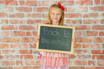 School enrollment - cute girl with chalk board is looking at camera and smiling.
