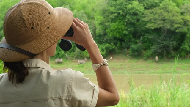 young people watch and photograph wild elephants on a safari tour in a national park. rear view tourist girl looking through binoculars at tropical animals in the African savannah. girl in safari hat