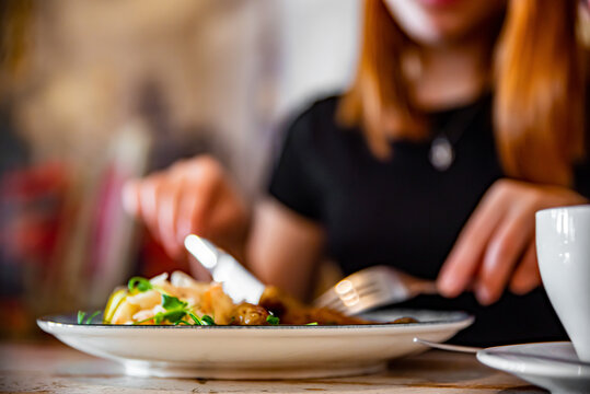 blurred woman hands with fork and knife eating food in cafe