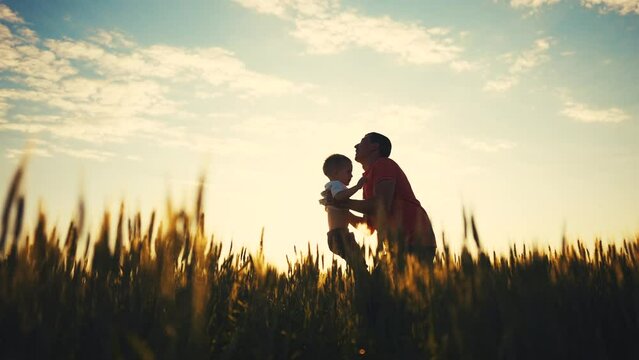 father playing with son in the park. dad throws baby up into the sky silhouette in the field in nature in the park. happy family kid concept. father dream day. baby boy playing with father silhouette