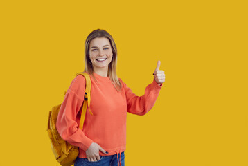 Happy content beautiful high school, college or university student girl with backpack standing on colour background, looking at camera, smiling and doing thumbs up. Education and success concept