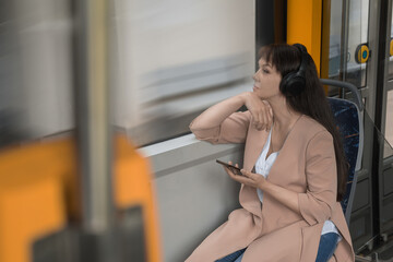 female passenger sitting with headphones and smartphone while moving in a tram, enjoying a ride on public transport