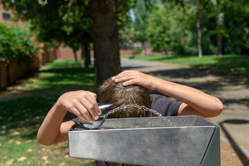 Boy wets his hair in a fountain in the street. Concept oh heat wave