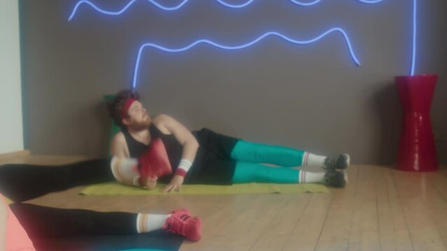 Tracking right of young and healthy Caucasian women and man in retro outfits lying on workout mats in studio at daytime