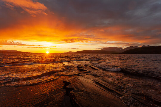 Midnight sun on the sea shore in Norway. Sunset over the coast. Small waves and a strong reflection on the water.