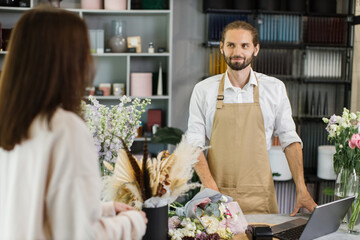 Young woman buys a beautiful bouquet of flowers in bearded male florist in cozy flower shop. Floristy and bouquet making in a flower shop. Small business.