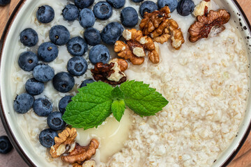 Close up of bowls with oatmeal porridge with ripe blueberries, nuts and honey for breakfast