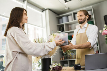 Back view portrait of young woman, buys a beautiful bouquet of flowers for party or holiday, and handsome man florist in a cozy flower shop. Floristics and making bouquets in a flower shop.