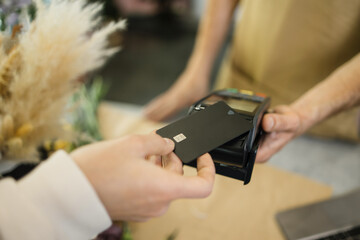 Close-up shot of unrecognizable male customer paying for her purchases with credit card in flower...