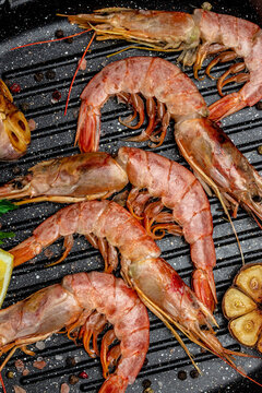 Grilled tiger shrimps with spice, lemon and garlic in a frying pan on a dark background. Prawns fried, Seafood appetizer vertical image. top view