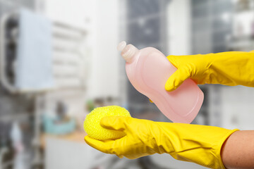 Women's hands in protective gloves with bottle of dishwashing liquid.