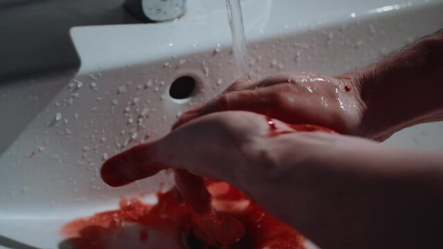 Handheld shot man washing bloody hands in bathroom sink. Horror thriller scene of hands covered in blood under running water. Murder concept, cinematic slow motion