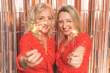 blonde Caucasian happy two women holding sparklers and celebrating New Year medium closeup indoors...