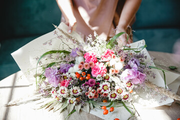 A woman florist packs a multi-branch bouquet in white paper on the table in her flower studio. Only...
