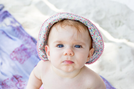 Close up portrait cute little baby girl with blue eyes in summer panama on background of white sand and plaid.
