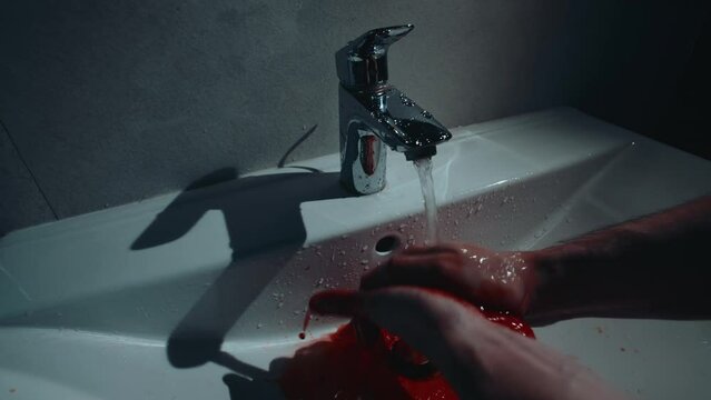 Handheld shot man washing bloody hands in bathroom sink. Horror thriller scene of hands covered in blood under running water. Murder concept, cinematic slow motion
