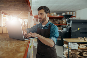 Warehouse worker in uniform standing on coffee small factory with laptop