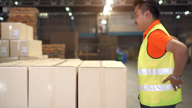 Asian man worker in a warehouse have an accident while carrying a heavy cardboard boxes with careless.