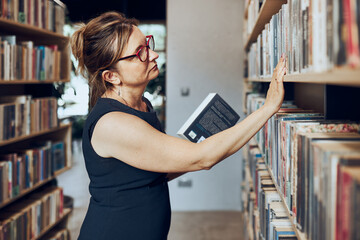 Woman looking for books in public library. Teacher searching for literature for reading and learning. Woman standing among bookshelves. Benefits of everyday reading