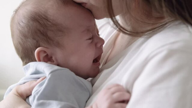 Mommy tries to calm the crying baby, shakes him in her arms, Dissatisfied, crying, upset, sad Newborn baby boy on mother hands at home