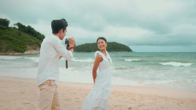 Happy young couple wearing white dress enjoy taking photo on the beach on holidays, travel, romantic, wedding concept