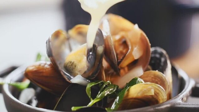 Chef pours sauce over mussels.
