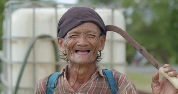 Happy smiling Asian male farmer more than sixty years old with a syringe tank on his back and works as a wage earner in a farm,smiling and laughing happily.