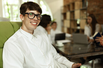 Young smiling man in official clothes and glasses, working at stylish modern office