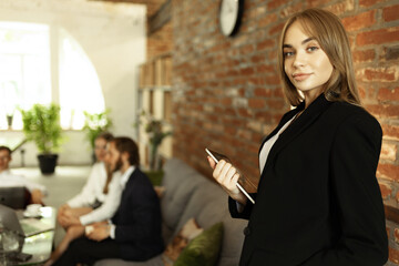 Portrait of young woman, office manager, employee in official suit working at modern work studio. Making project presentation