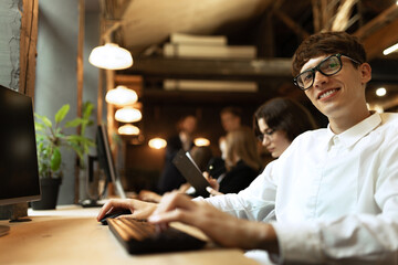 Young smiling man, office employee working on computer on new project. Modern office background.