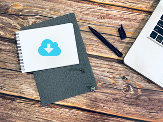 A download icon printed on notebook and pen on wood