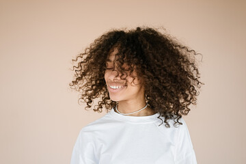 Joyful happy woman with curly hair dances carefree enjoys moment shakes her head isolated over brown background with blank space for your advertisement      
