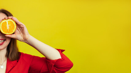Portrait of a Caucasian girl with a radiant clean skin holding orange halves isolated on a yellow background. The concept of cosmetics with vitamin C. A place for your advertising or text.