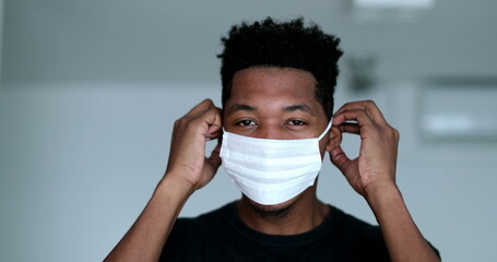 Young black man putting and adjusting surgical face mask