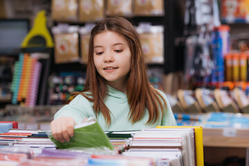 smiling girl near blurred multicolored copybooks in stationery store.