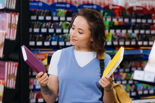 smiling tattooed student choosing copybooks in blurred stationery store.