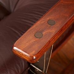 Elegant burgundy brown leather reclining Norwegian design chair. Armrest detail view with wooden floor.