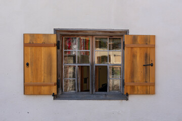 Holzfenster an einem alten Haus, kleinteilige Gläser in alten Fenstern mit braunen Holzläden in einer weissen Hauswand