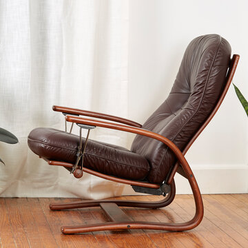 Elegant Burgundy Brown Leather Reclining Norwegian Design Chair. Side View With Luxurious White Curtains And Wooden Floor.