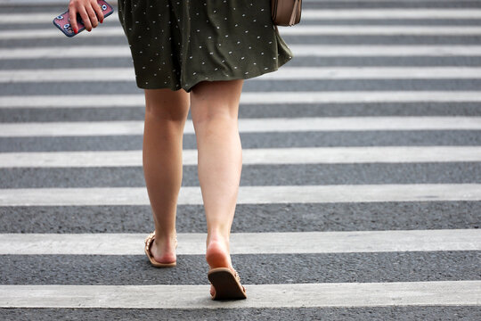 Woman in summer dress crossing the street, female legs on pedestrian crossing. Concept of road safety