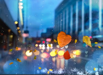 Rainy Autumn leaves on window rain drops and modern  city buildings panorama , traffic blurred light colorful reflection cold season defocus background 