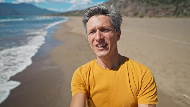 happy middle aged greyhead man takes selfie at sea coast with waves enjoying sunny day on beautiful beach Iztuzu in Turkey. inspired enjoyed man makes video call and talks about his place
