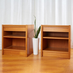 Product photo of two light wooden Danish Modern nightstands staged on a wooden floor with a houseplant between them before luxurious white curtains	