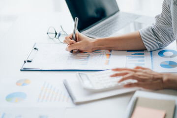 Young businesswoman analyzes cost graphs on desk in conference room with laptop