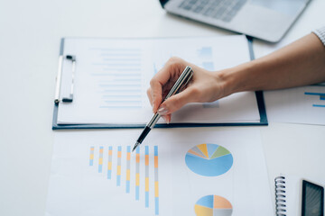 Young businesswoman analyzes cost graphs on desk in conference room with laptop