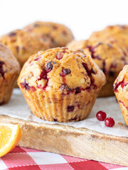Cranberry orange muffin on a wooden table with white background. Vertical shot, a closeup. Freshly baked vegan muffins with cranberries and orange juice. Sweet vegan breakfast, dessert, or snack.  - obrazy, fototapety, plakaty