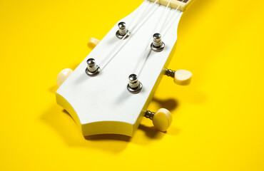 Close up neck of the guitar..White colored wooden ukulele guitar on the yellow background. Hawaiian Four String Guitar. Musical Instrument.